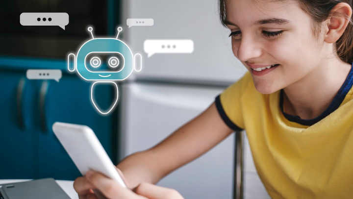 Jugendliche in gelbem T-Shirt sitzt an einem Tisch, hält ein Handy in beiden Händen und schaut lächelnd darauf. Eine Simulation oberhalb des Handys suggeriert, dass das Mädchen mit einer KI chattet.